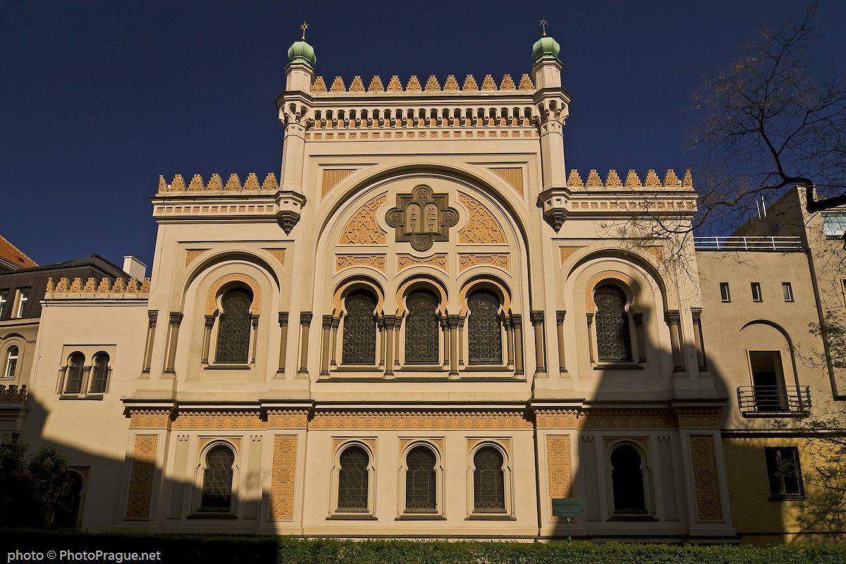 The facade of the synagogue, with its arches, geometric details, and small green domes against a blue sky.