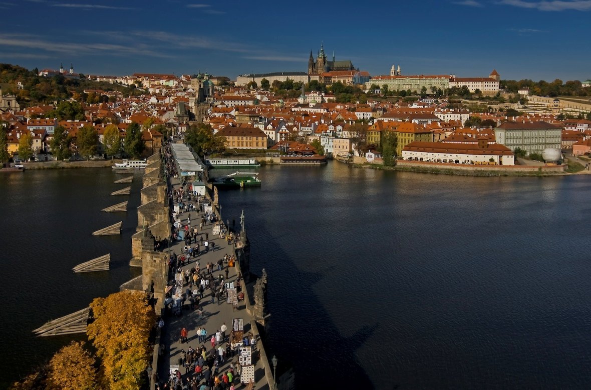 Charles Bridge seen from above and teeming with people spans the river and leads to the majestic Prague Castle