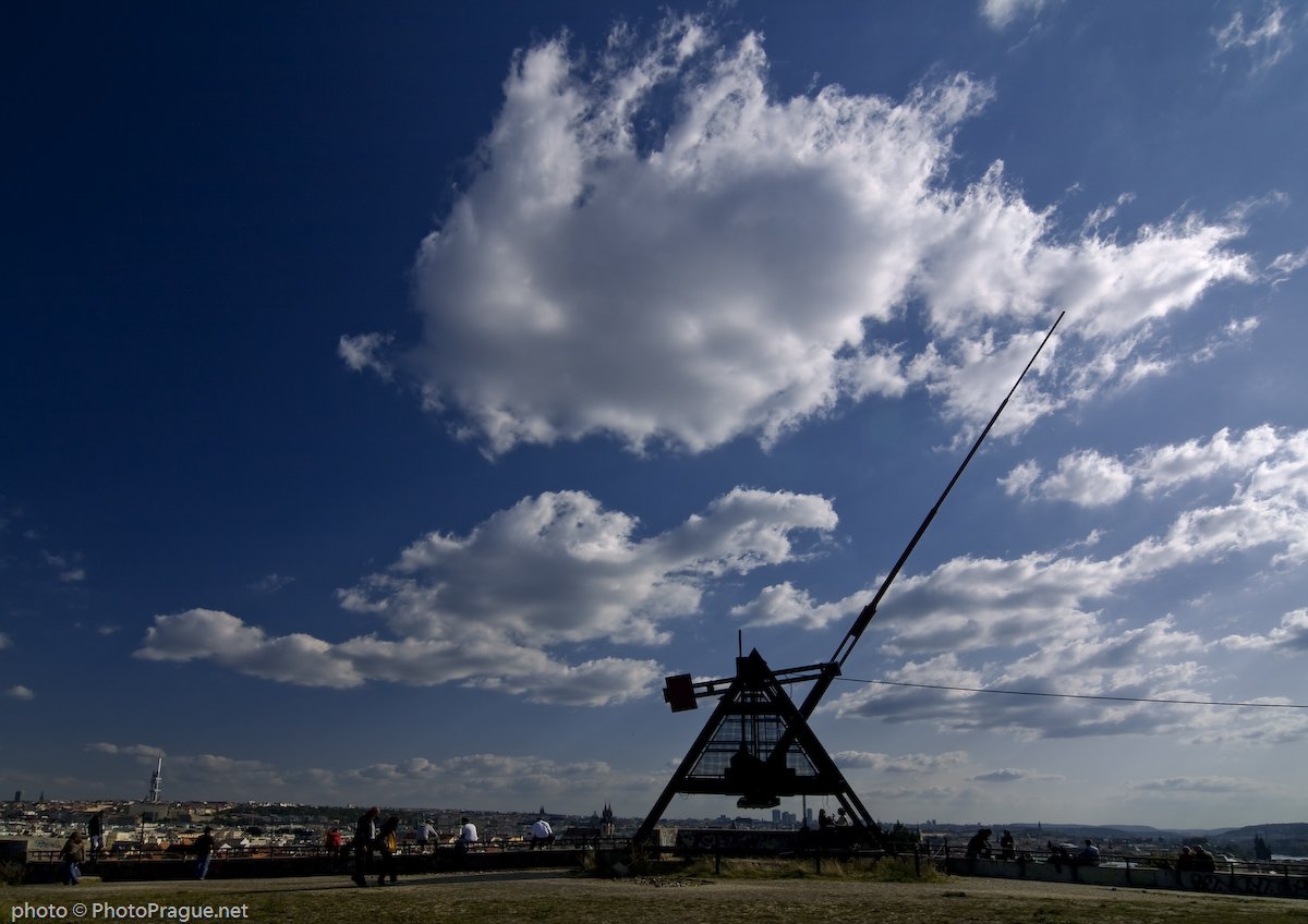 A very large metronome with a blue sky and a few clouds