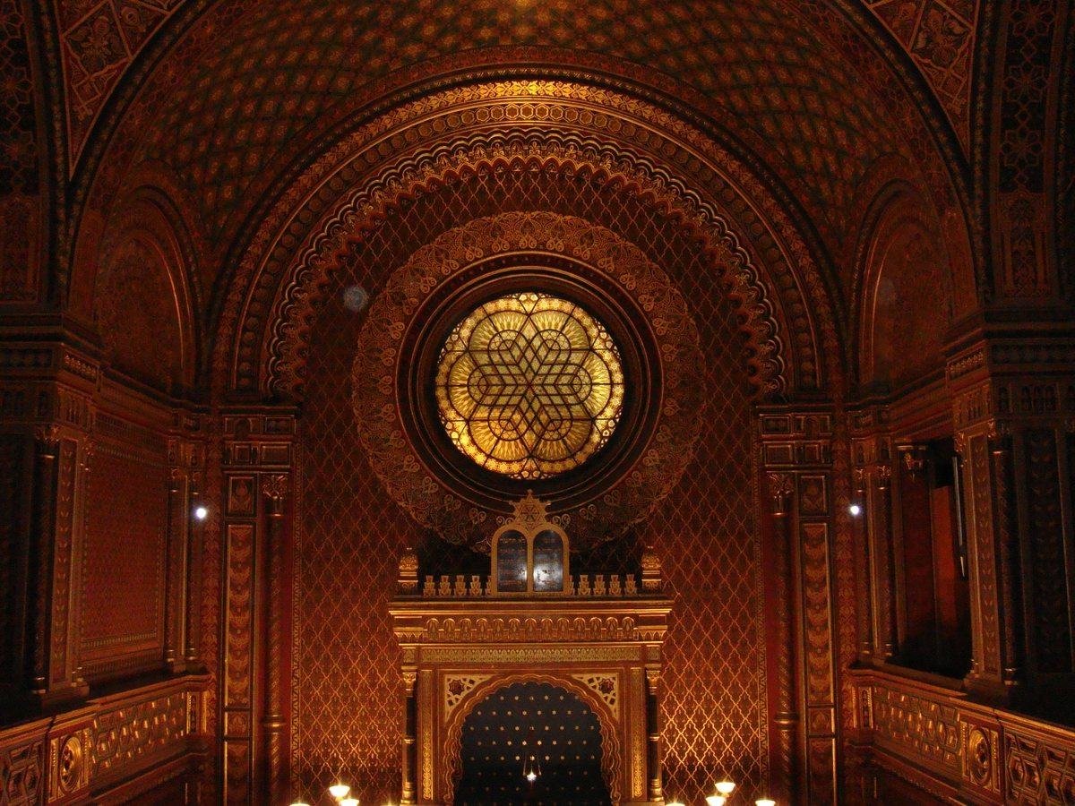a monumental hall, bathed in golden twilight, with walls and stained-glass windows adorned with carved motifs