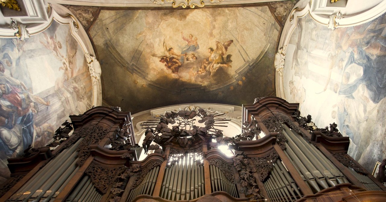 A large organ surrounded by large paintings on both sides of the walls and the roof