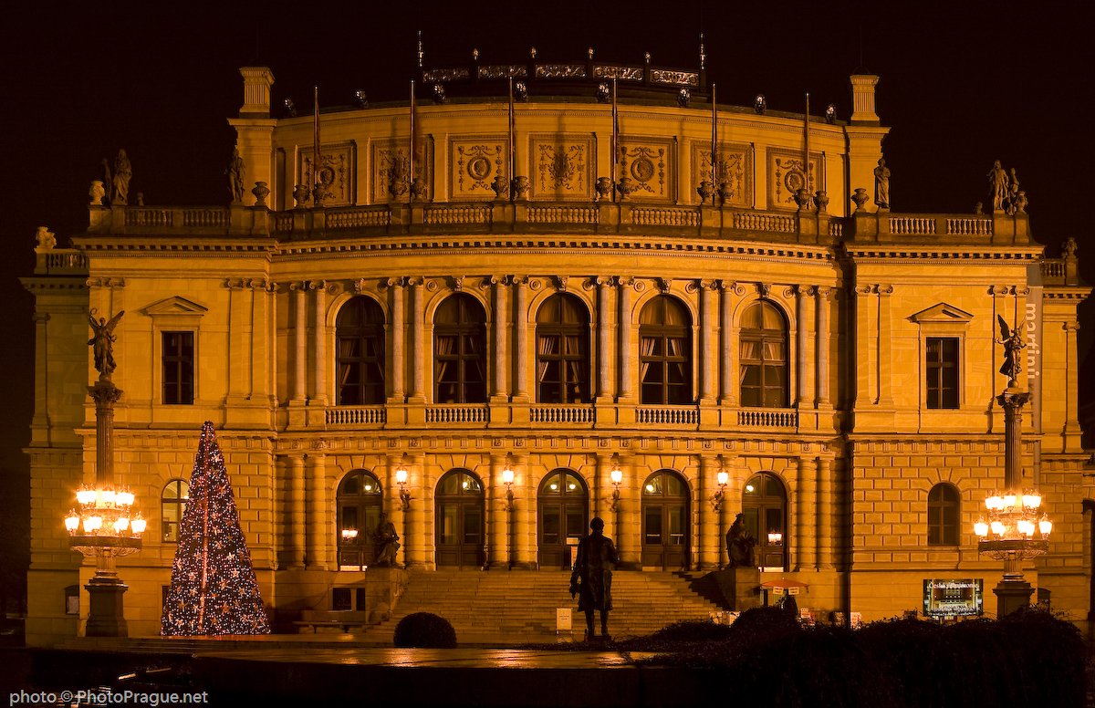 A large building with two stories, each featuring five windows, and a fir tree just to the left