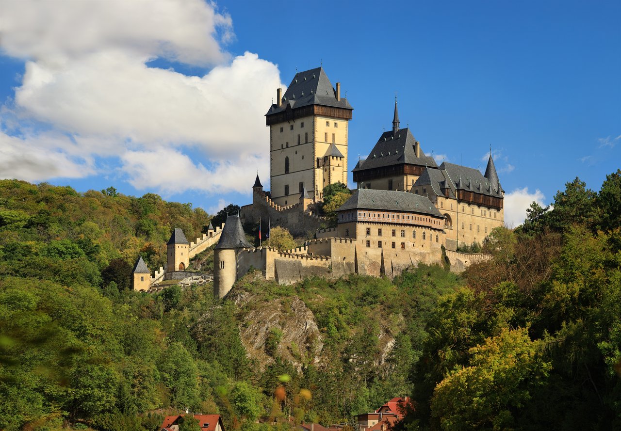 A beige Gothic fortress with five small towers and black roofs, situated on a hill